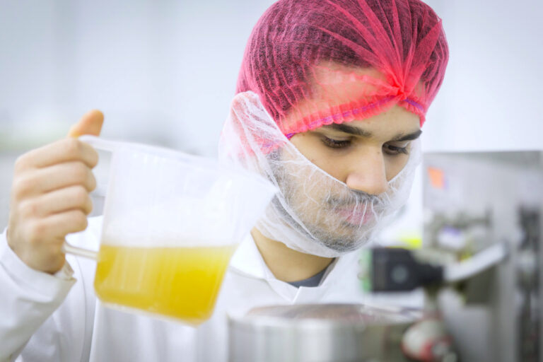 Man holding jug of fluid dressed in PPE appropriate to a kitchen