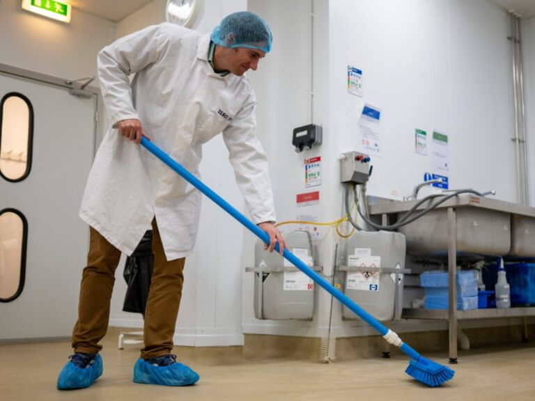 Food production worker in PPE sweeping a floor