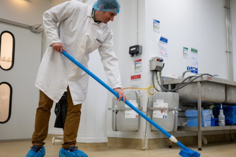 Food production worker in PPE sweeping a floor